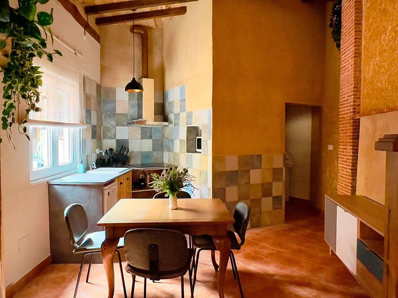 Comedor con mesa de madera, sillas y cocina al fondo