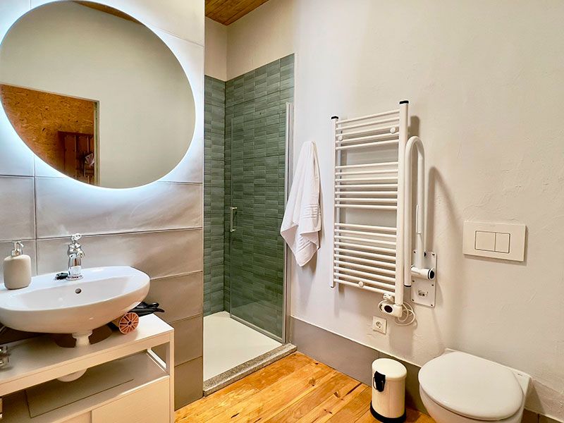 Baño con inodoro, radiador secador, lavabo y espejo redondo