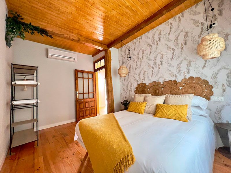 Cama de matromonio con acabados en mimbre, pared con papel pintado y techo de madera